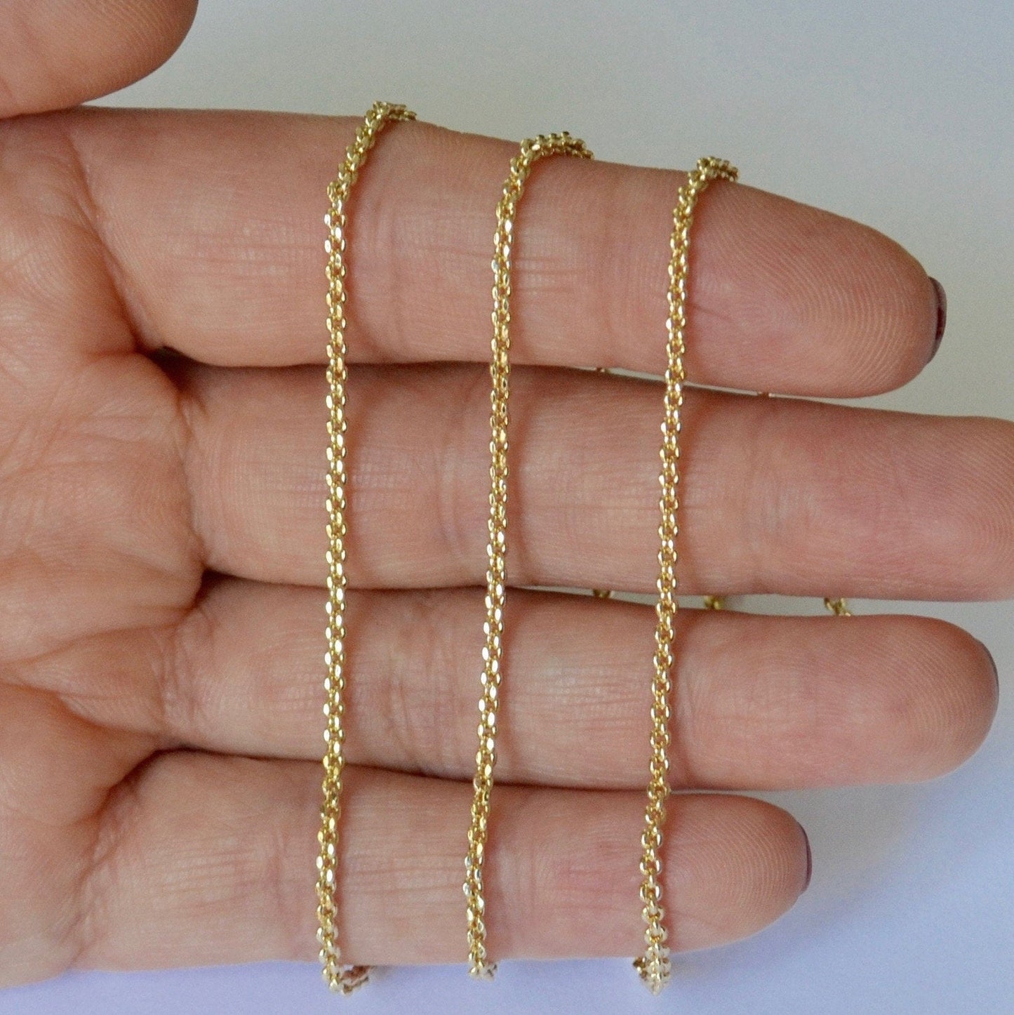 Gold cable chain held between fingers against a white background
