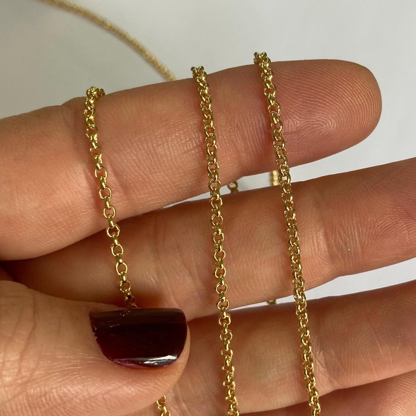 Dainty Gold chain necklace held between fingers against a neutral background