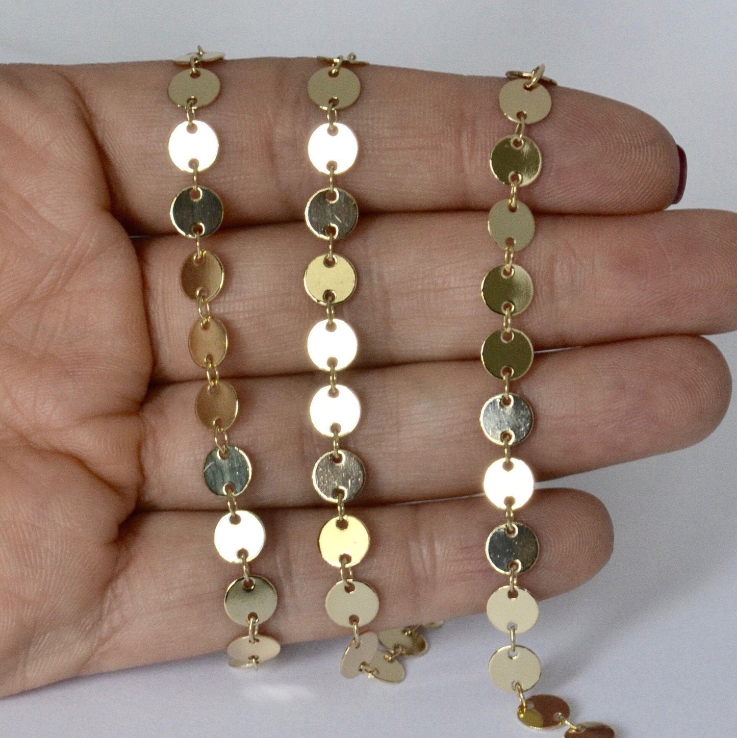 Gold coin chain necklace held in a hand against a white background