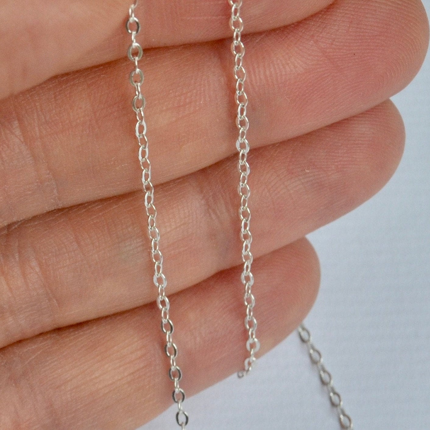 925 sterling Silver cable chain held between fingers against a neutral background