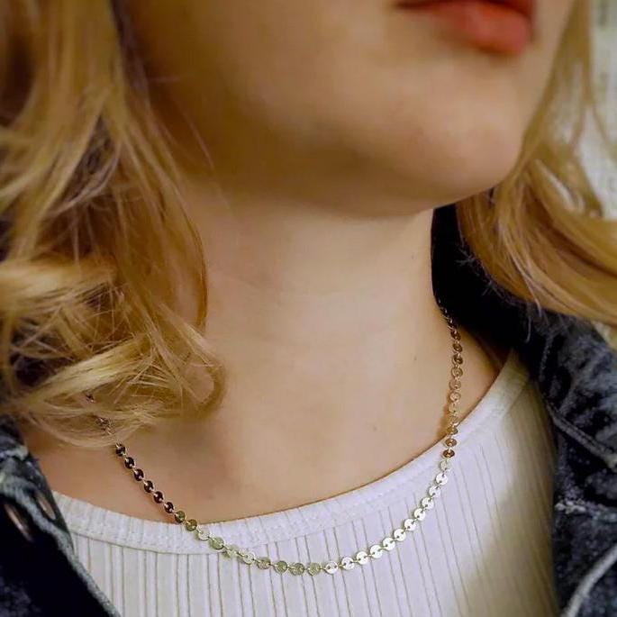 Close-up of a woman wearing a delicate sterling silver coin necklace with a blurred background