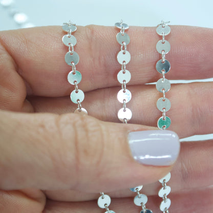 Silver coin chain necklace held between fingers with a blurred background