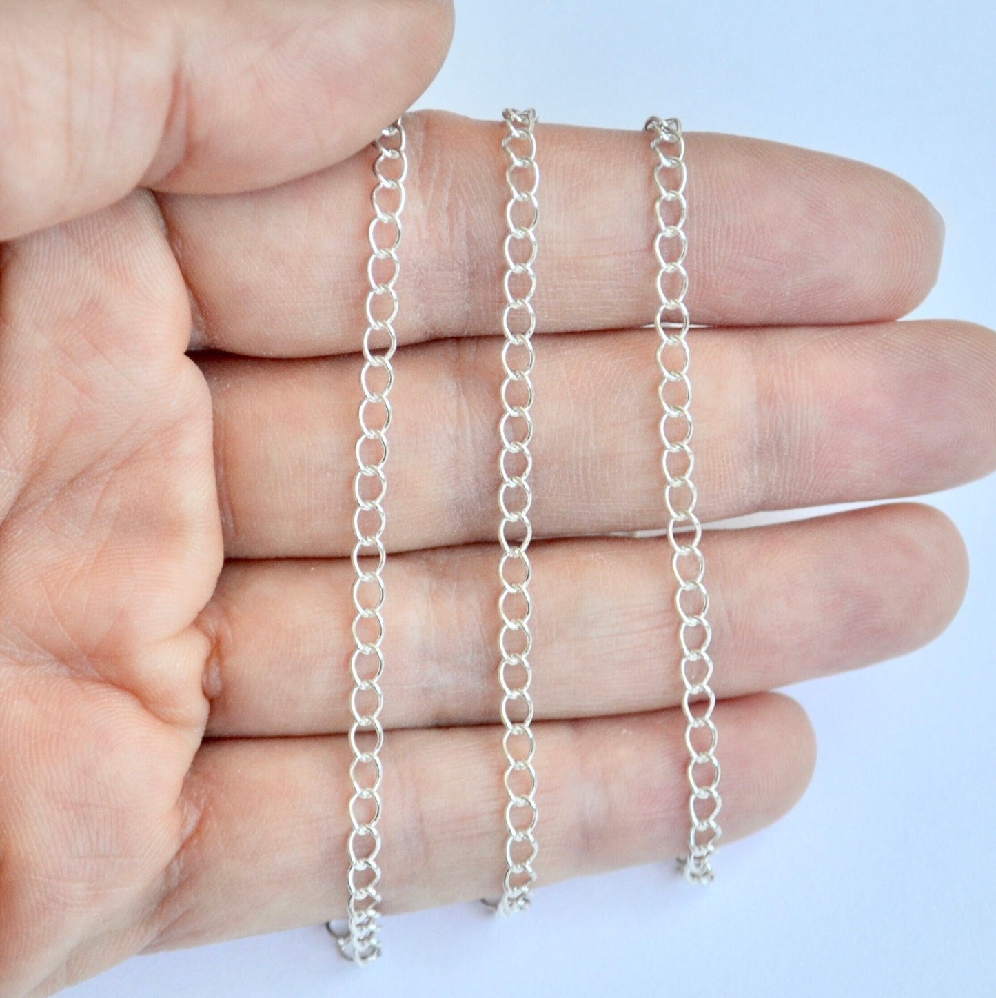 Sterling silver curb extender chains held between fingers against a light blue background