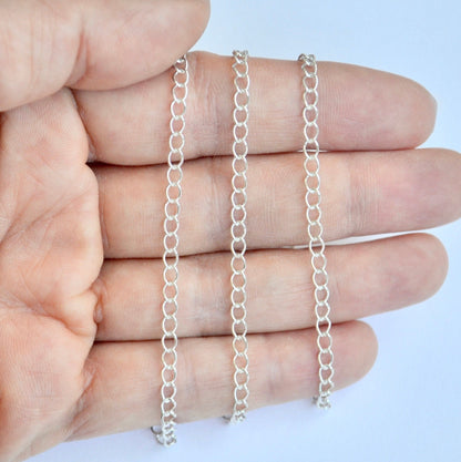 Sterling silver curb extender chains held between fingers against a light blue background