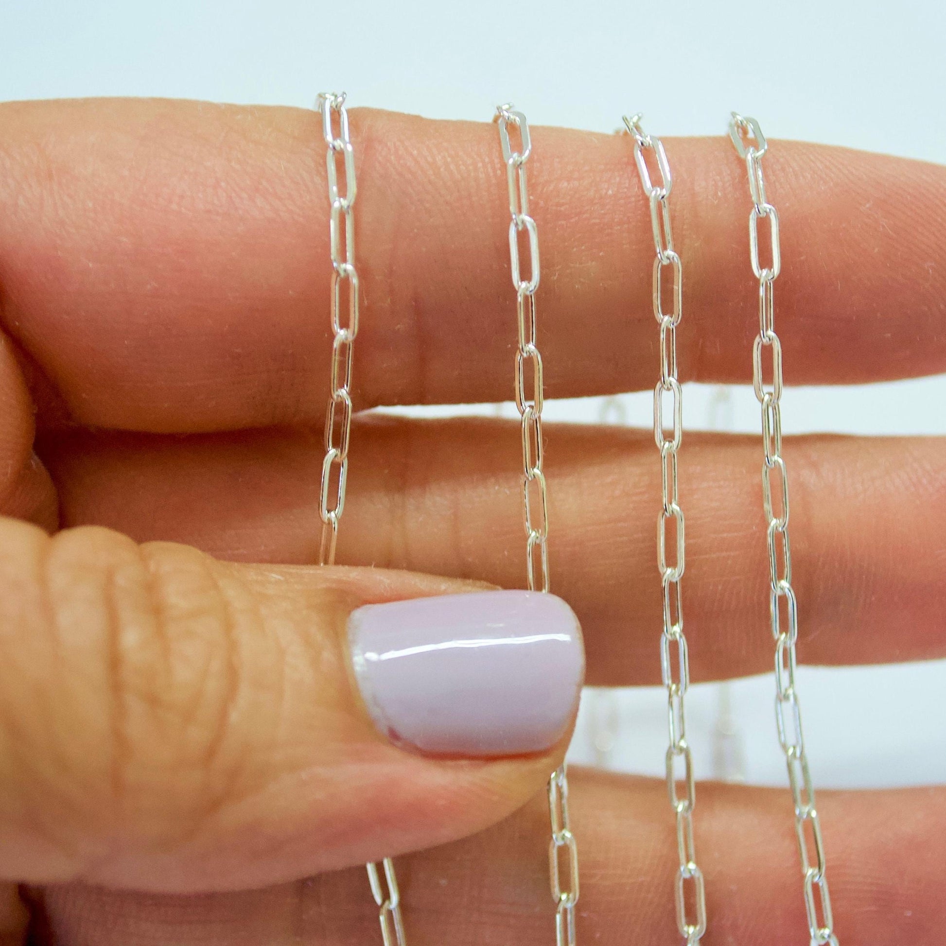 Silver chain held between fingers with a blurred background