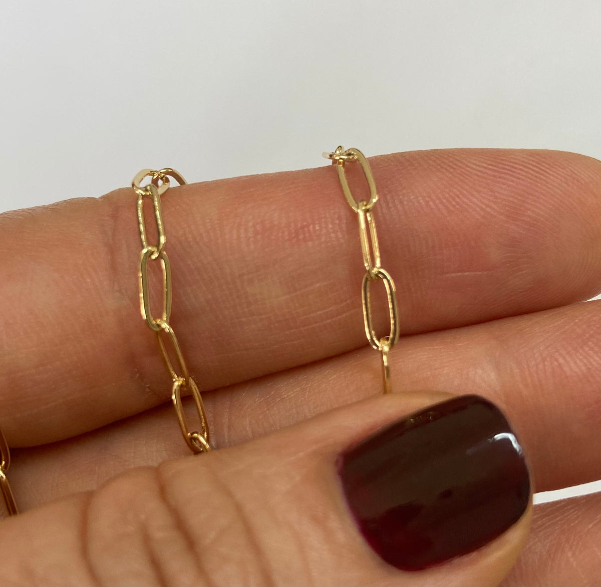 A close-up of a hand with a delicate gold paperclip chain, with the fingers displaying the thin chain links.