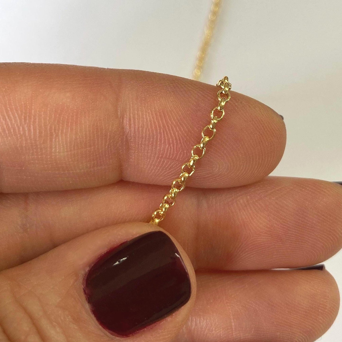 Gold Filled rolo chain held between fingers with a plain background