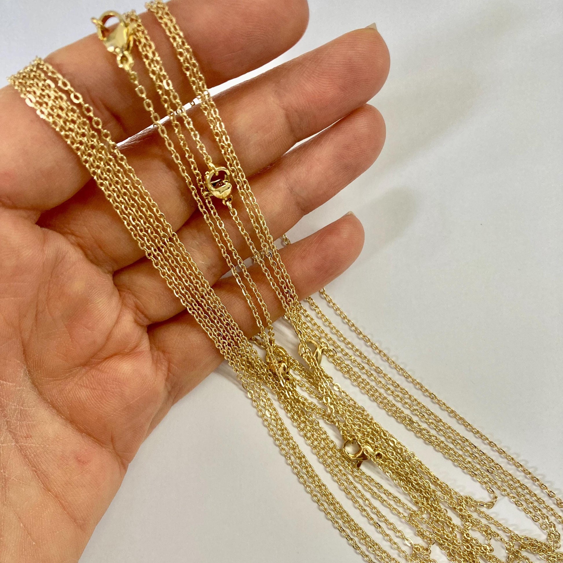 Hand holding multiple gold chains against a white background