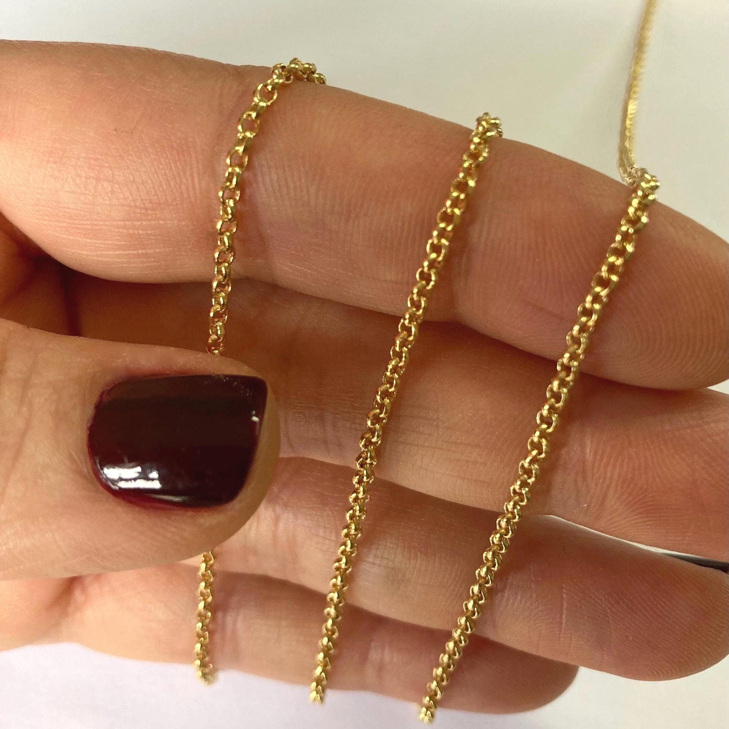 Gold chain rolo chain 2 mm held between fingers with a neutral background