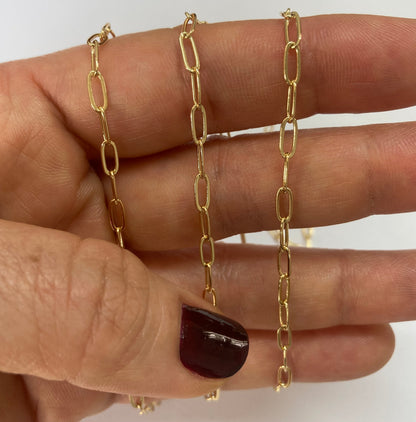 A close-up of a hand holding three parallel gold paperclip chain against a plain white background.