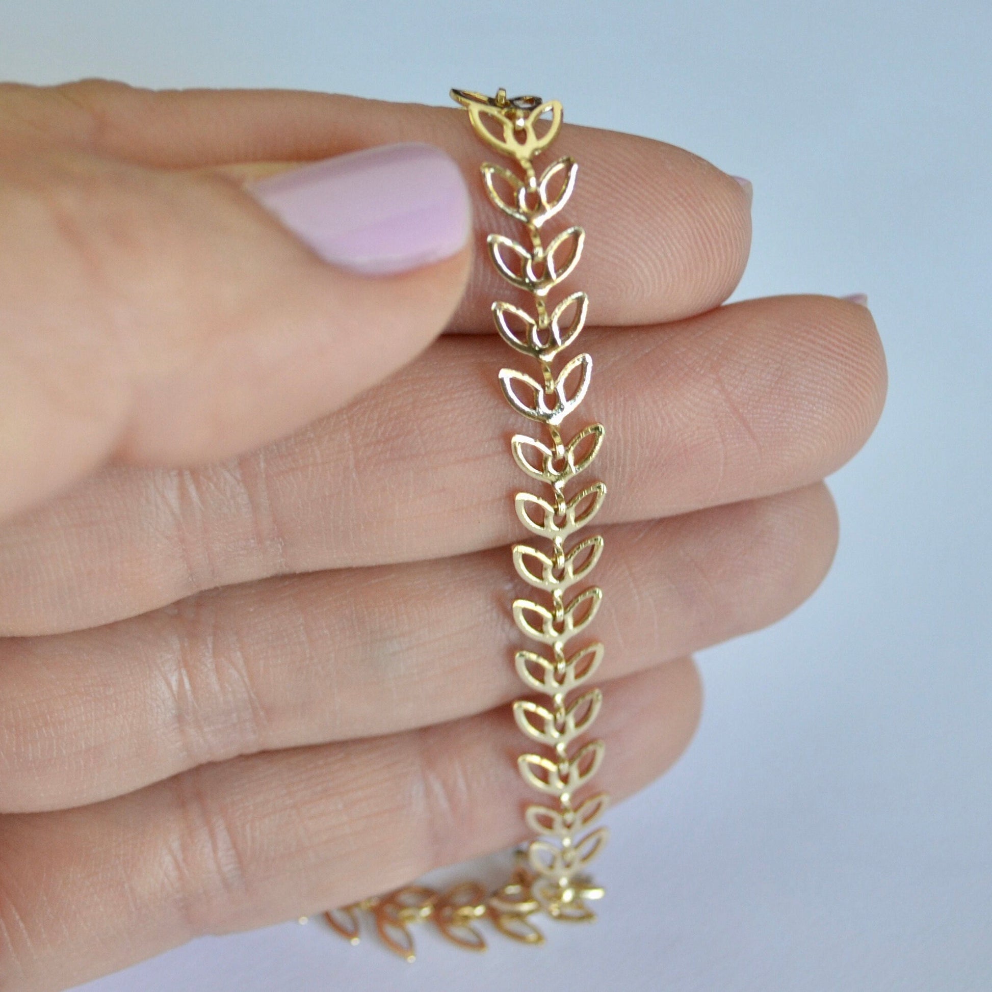 Gold filled bracelet with leaf design held between fingers against a light background