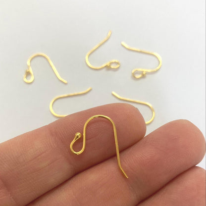 Gold earring hooks on a white background with a hand holding one hook.