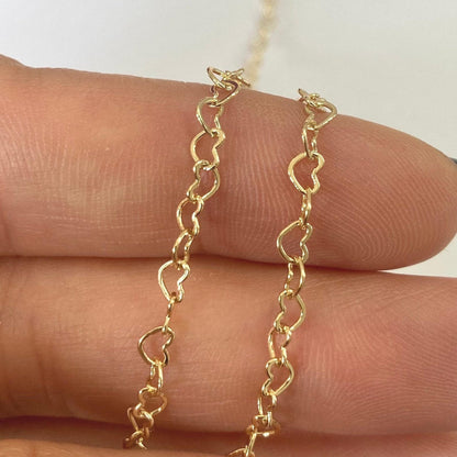 Gold filled heart shape chain on a person's hand against a white background
