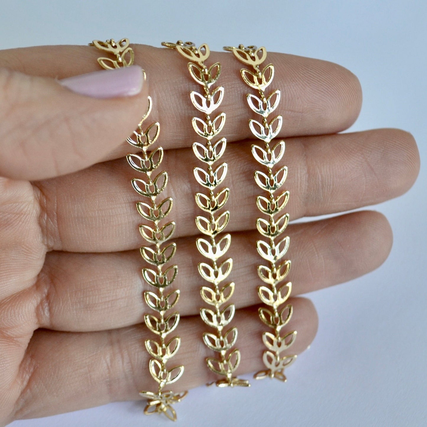 Gold filled leaf-shaped chain held between fingers against a light background