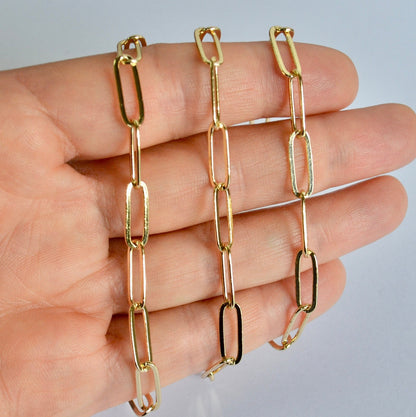 Gold filled long paperclip chain held by a hand against a neutral background