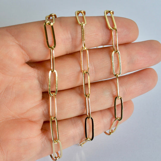 Gold filled long paperclip chain held by a hand against a neutral background