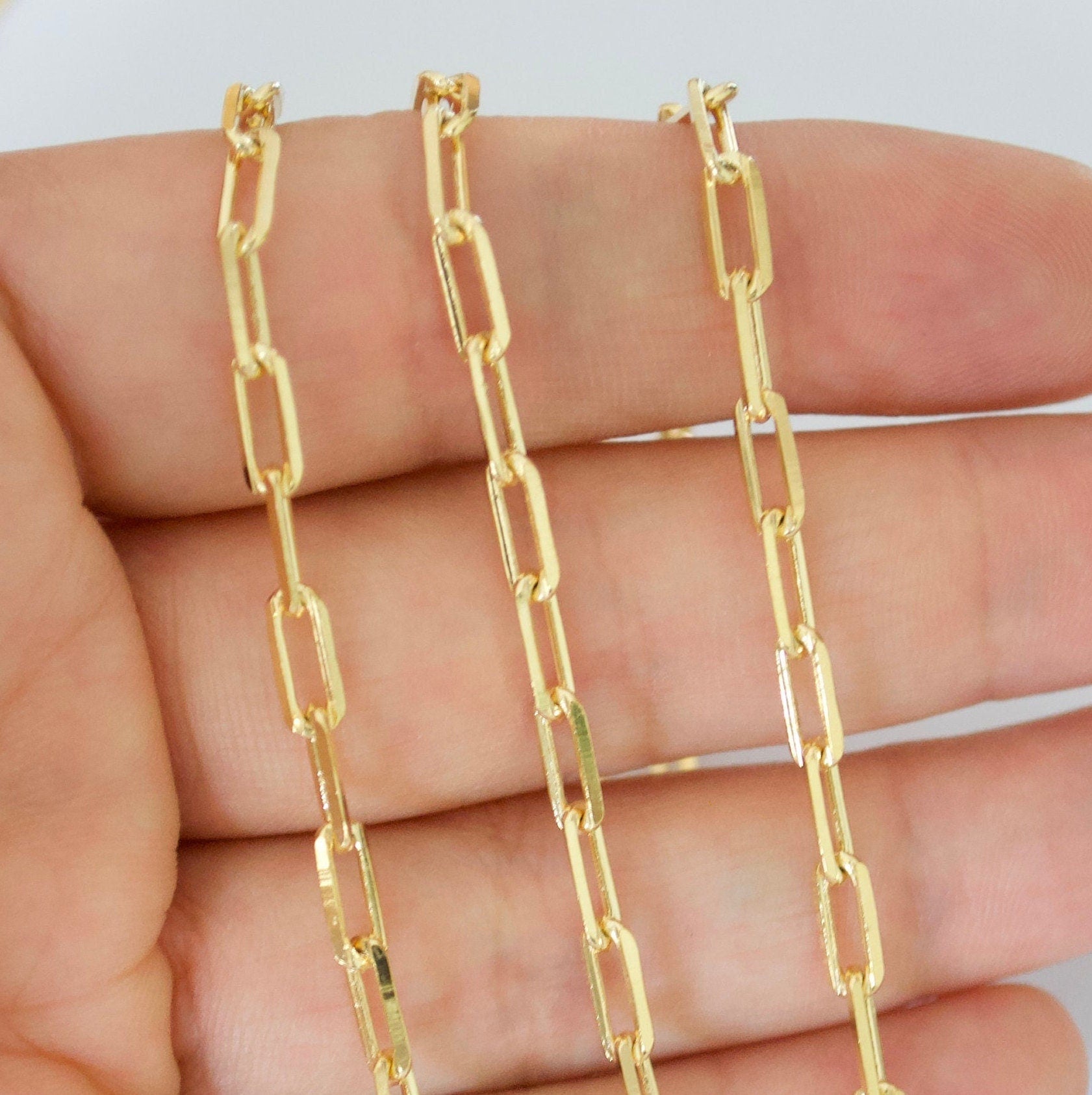 14k Gold filled paperclip chain held between fingers against a white background