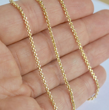 Gold filled cable chain held between fingers against a neutral background