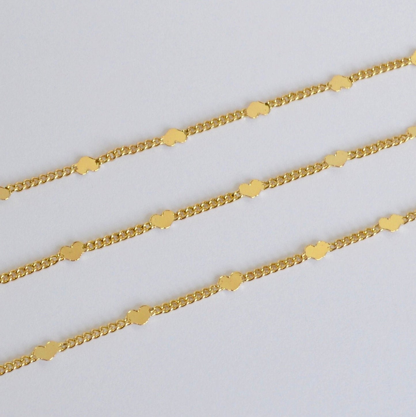 Three gold chains decorated with tiny hearts on a light gray background