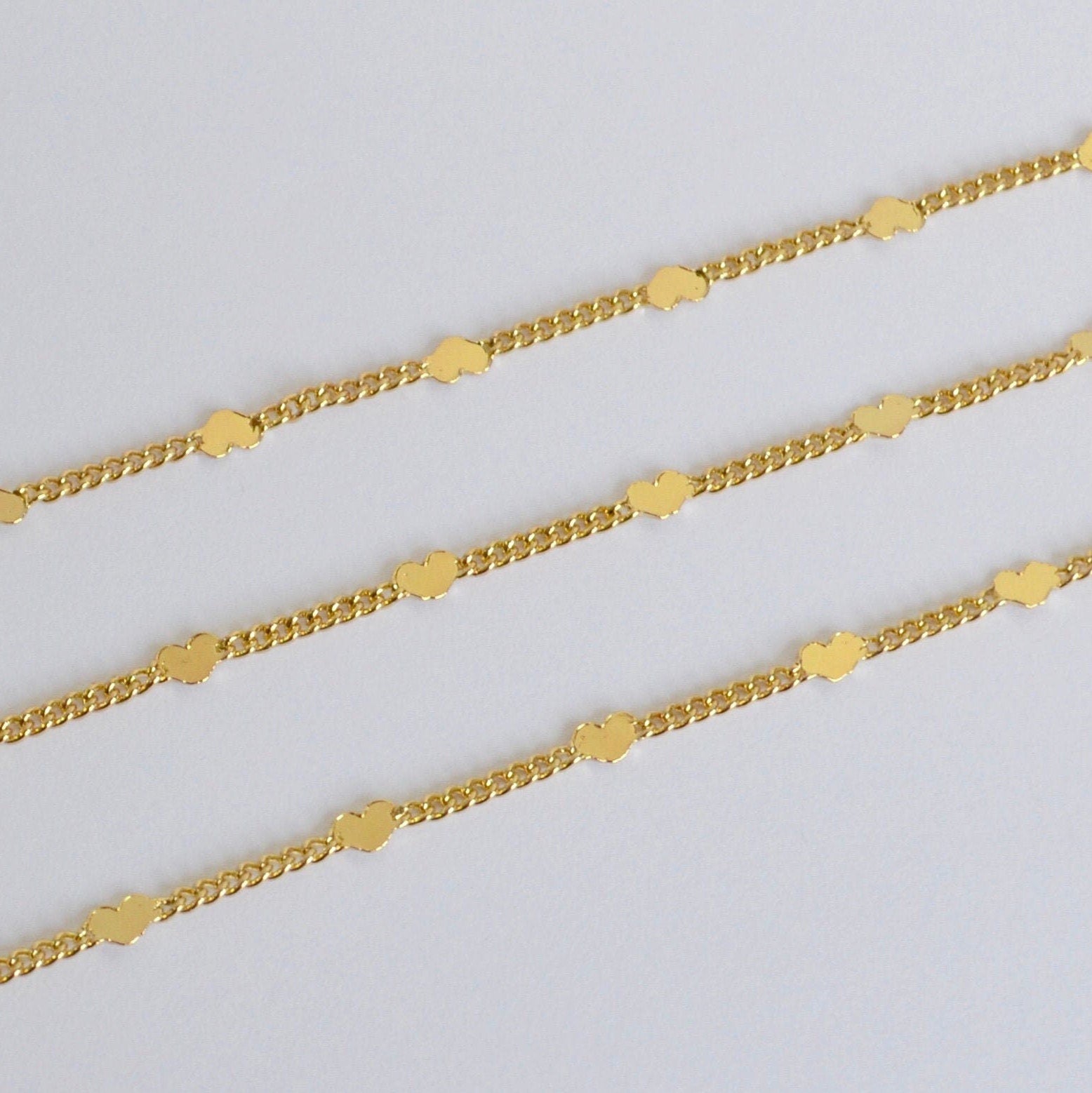 Three gold chains decorated with tiny hearts on a light gray background
