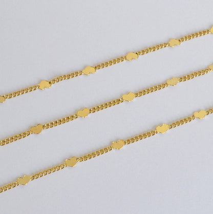 Three gold chains decorated with tiny hearts on a light gray background