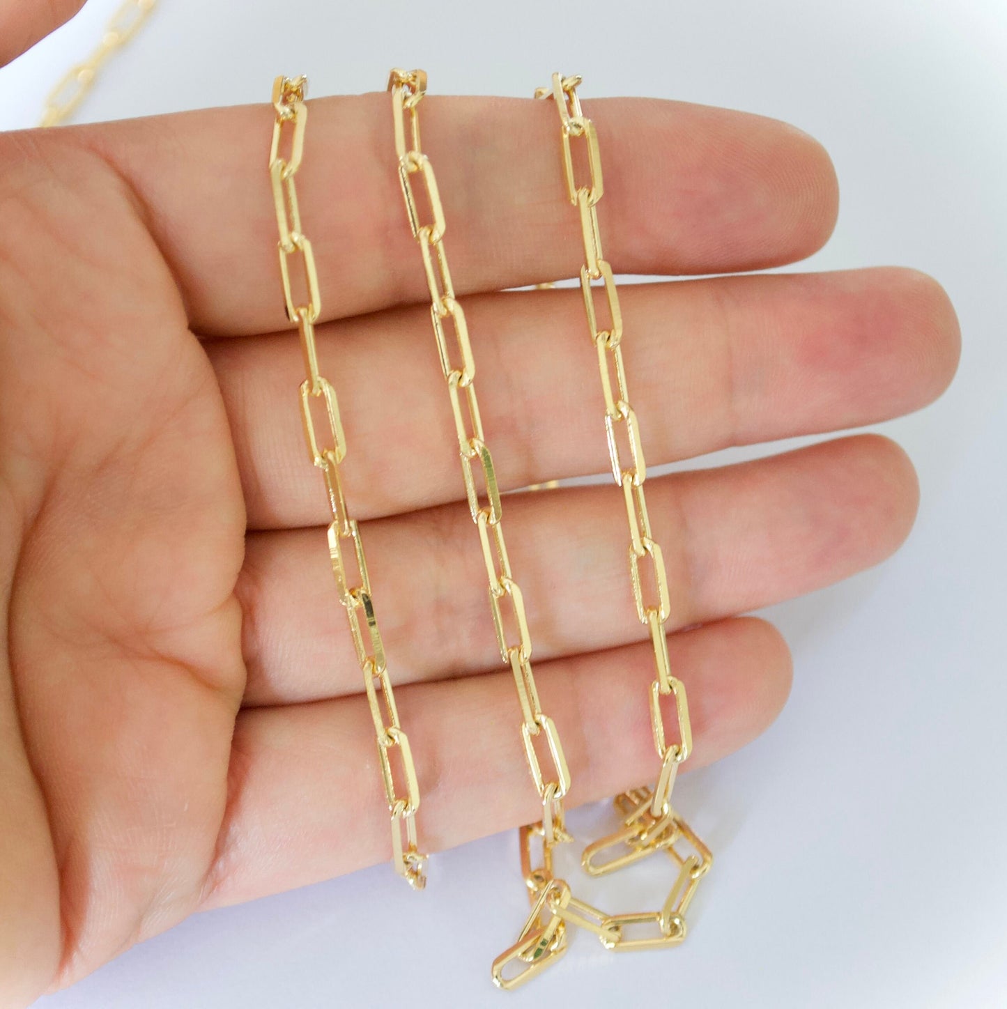 Gold paper clip chain held between fingers on a white background