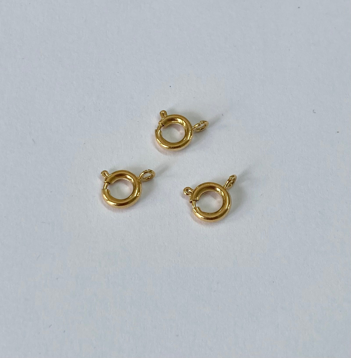 Three small gold filled spring clasps arranged on a plain light gray background.