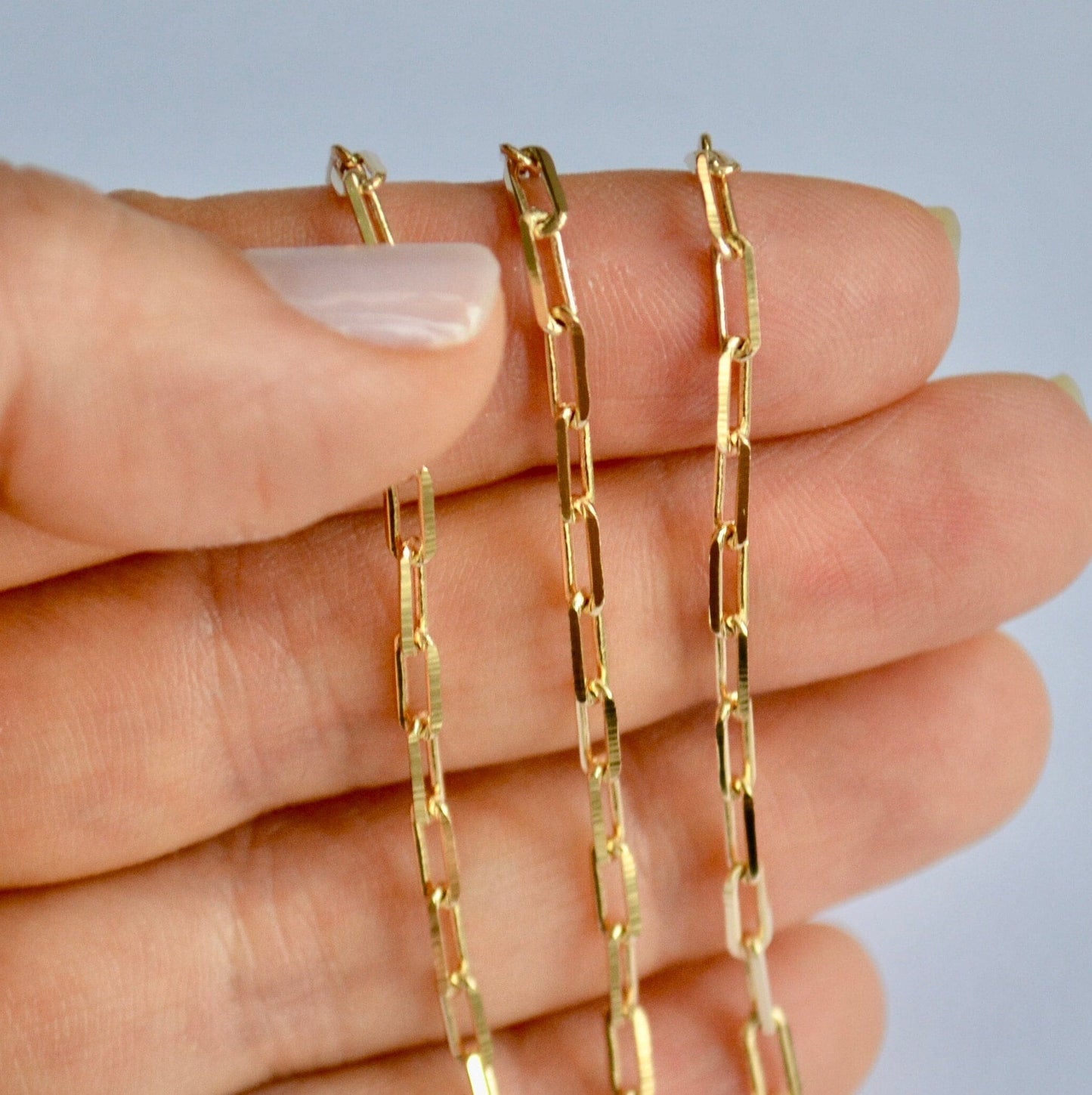 Gold filled paperclip chain held between fingers against a neutral background
