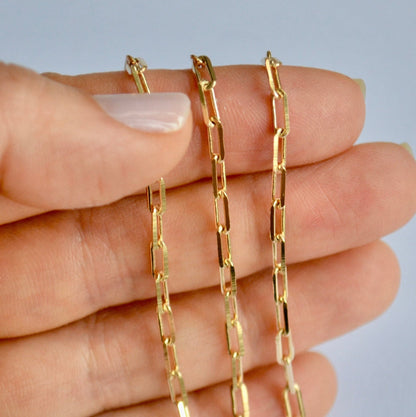 Gold filled paperclip chain held between fingers against a neutral background