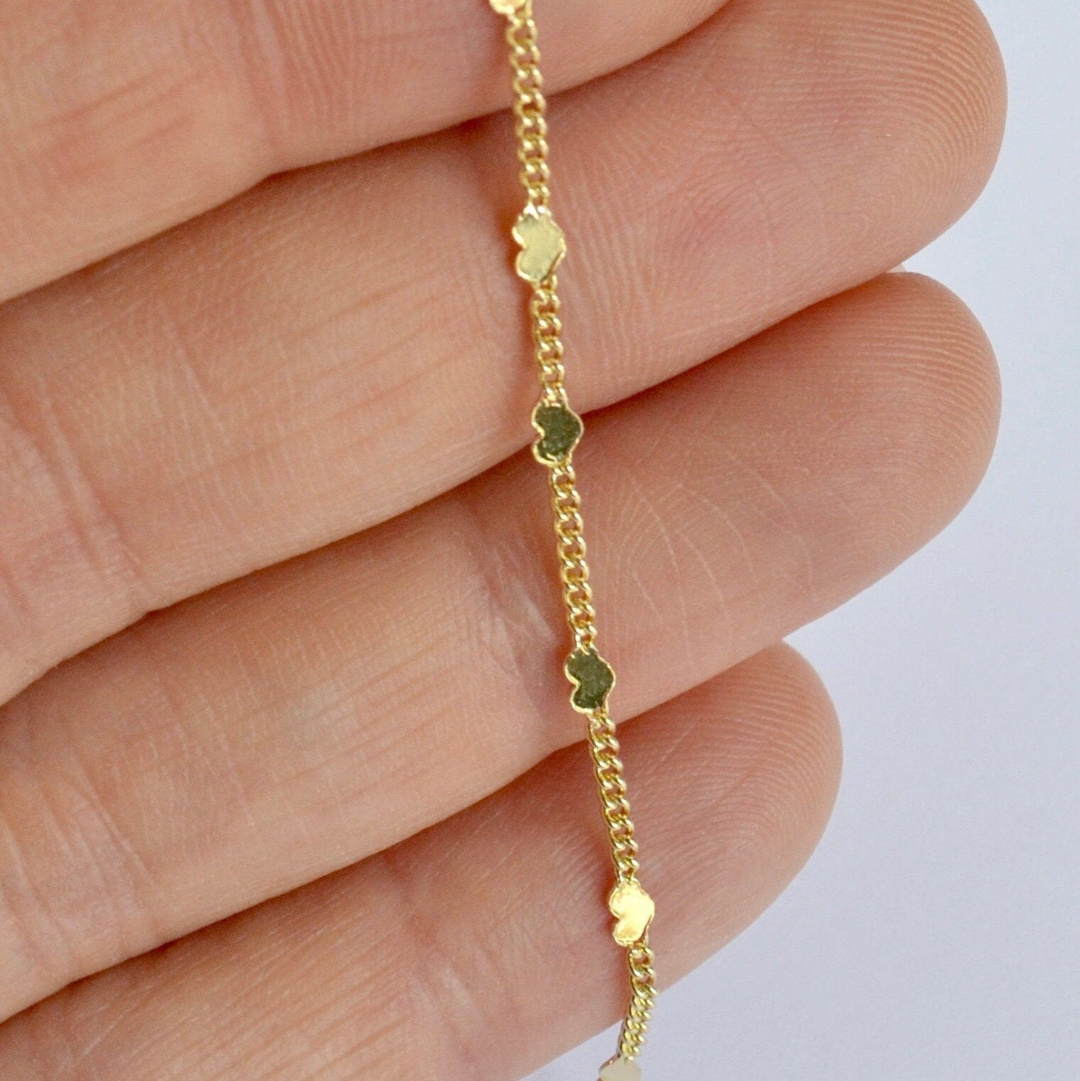 Gold bracelet with heart-shaped charms on a hand against a light background