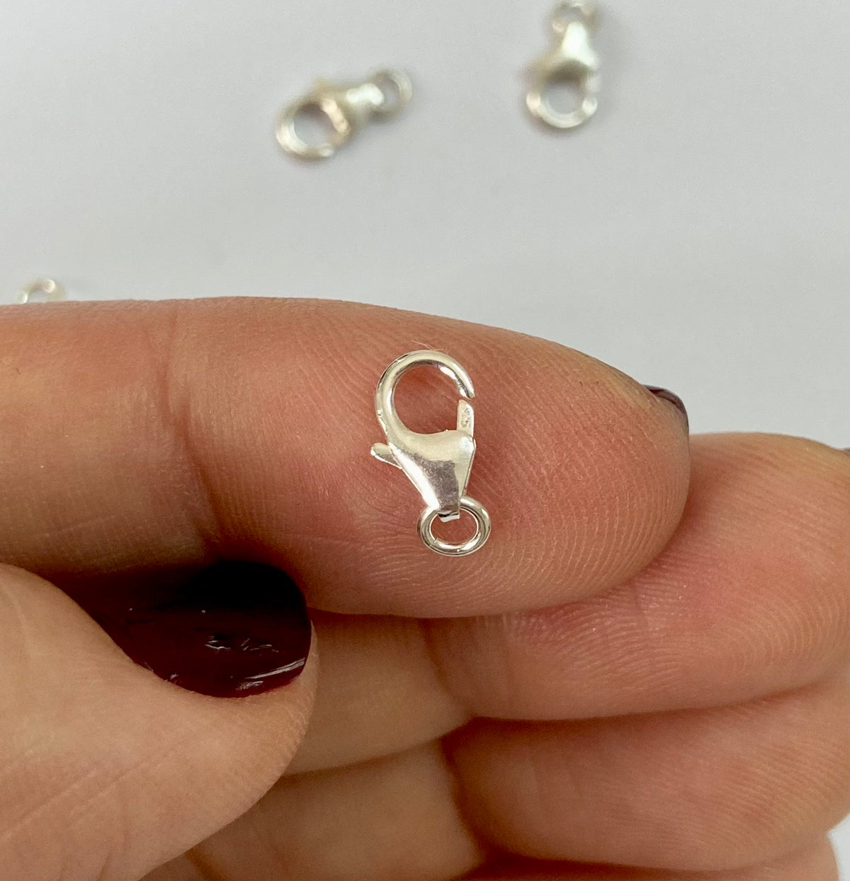 A sterling silver lobster clasp held between a person's fingers against a plain light background.