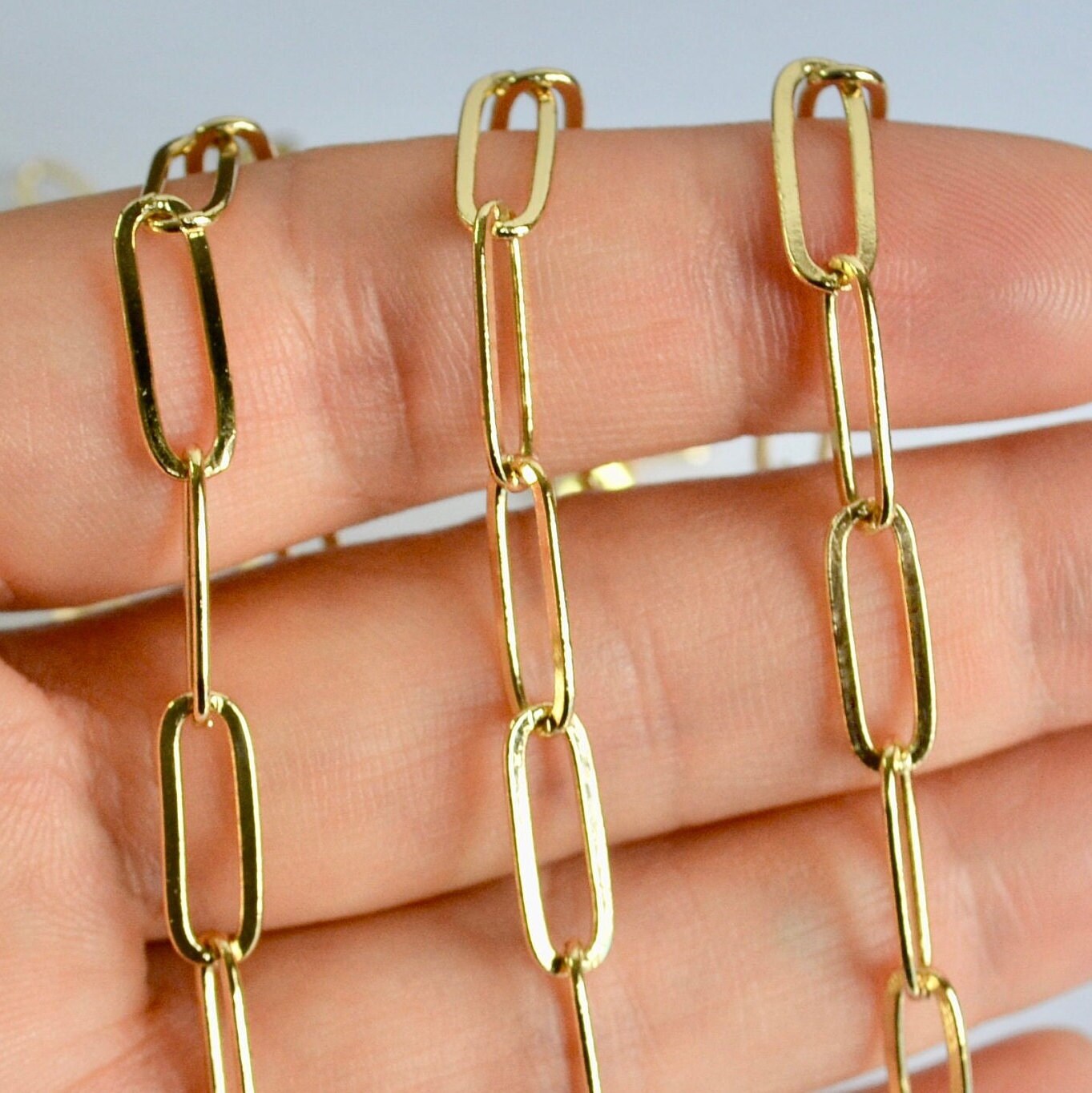 Gold filled elongated flat link chain necklace on a hand against a neutral background