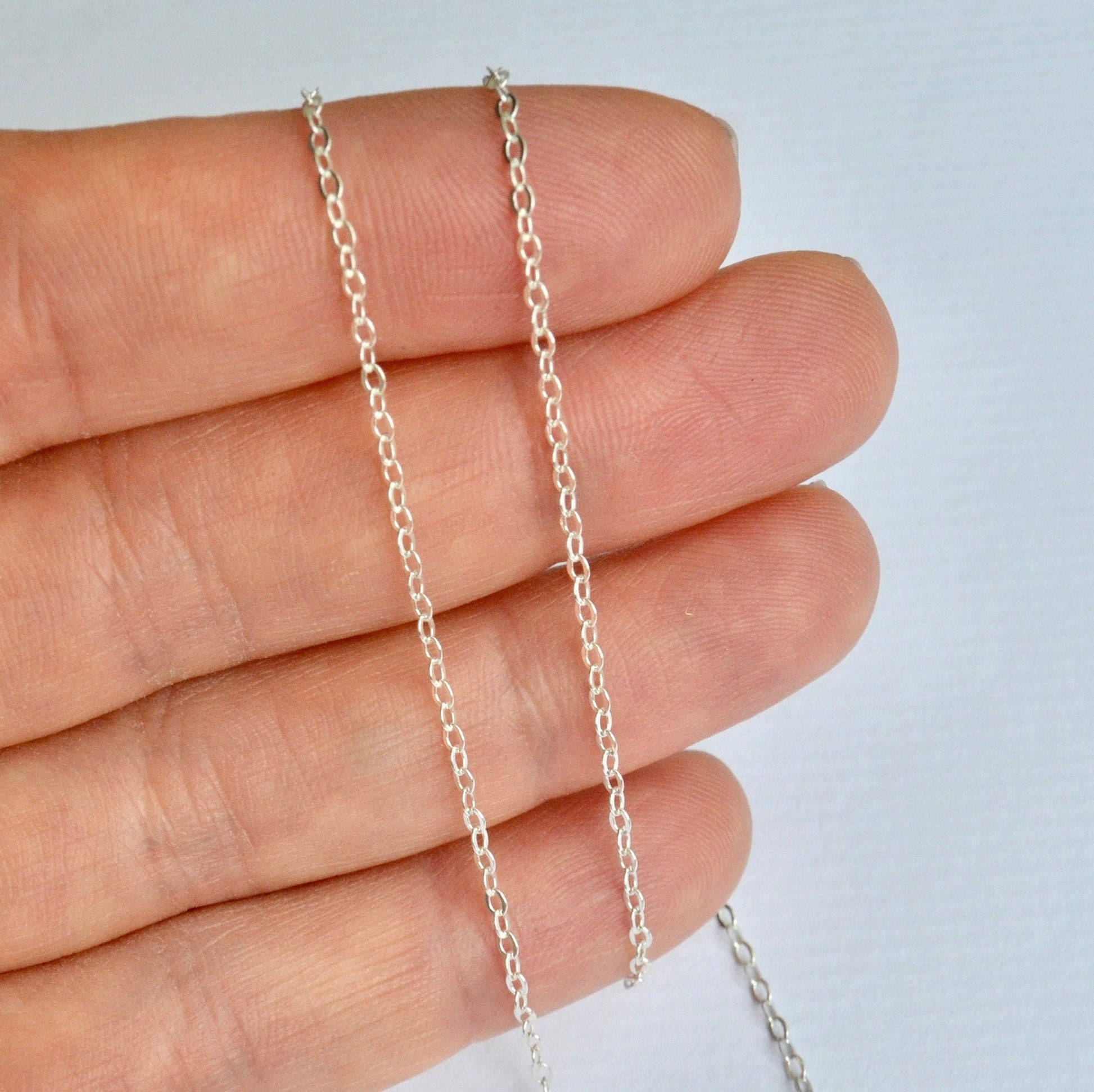 Silver cable chain held between fingers against a light background