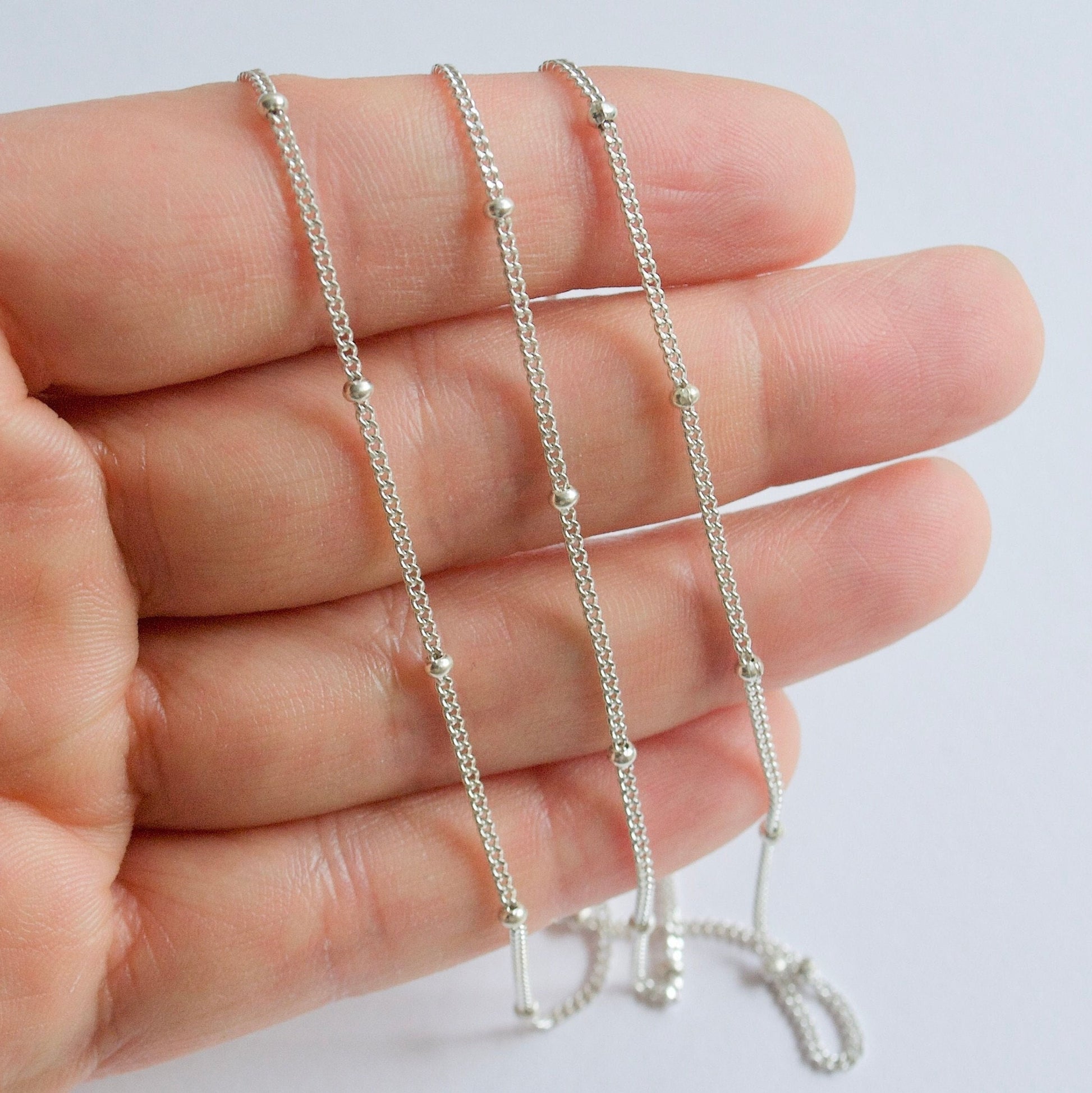 Sterling Silver satellite chain held between fingers on a light background