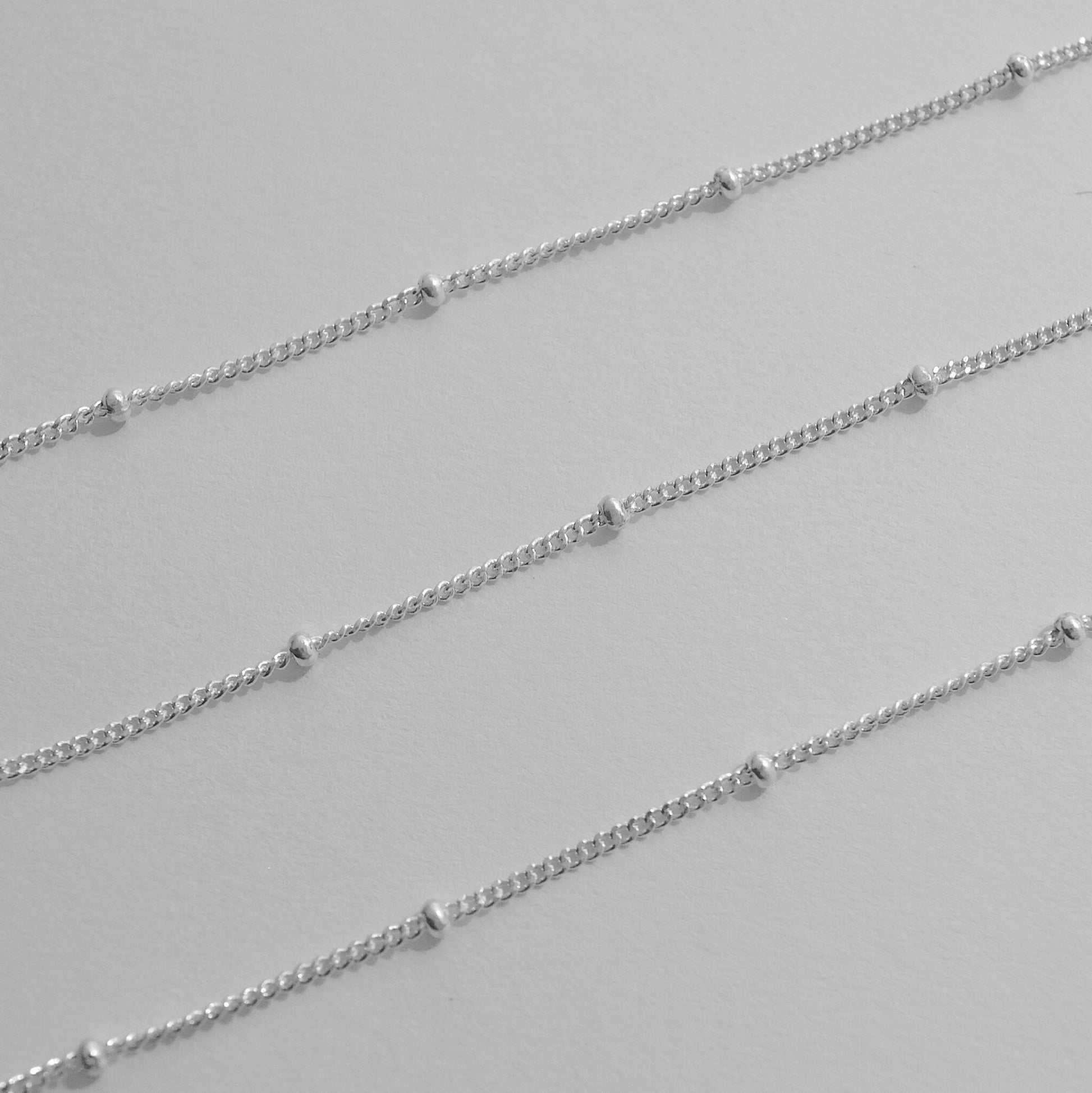 Silver satellite chain necklaces on a light gray background