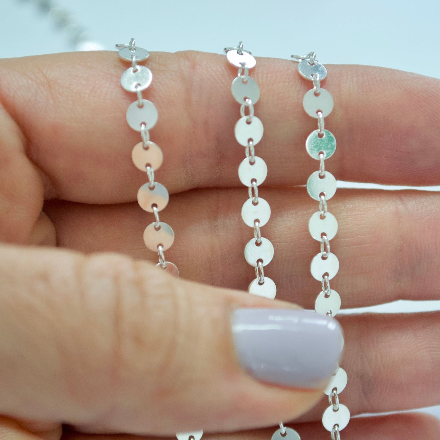 Silver sequin chain held between fingers with a blurred background