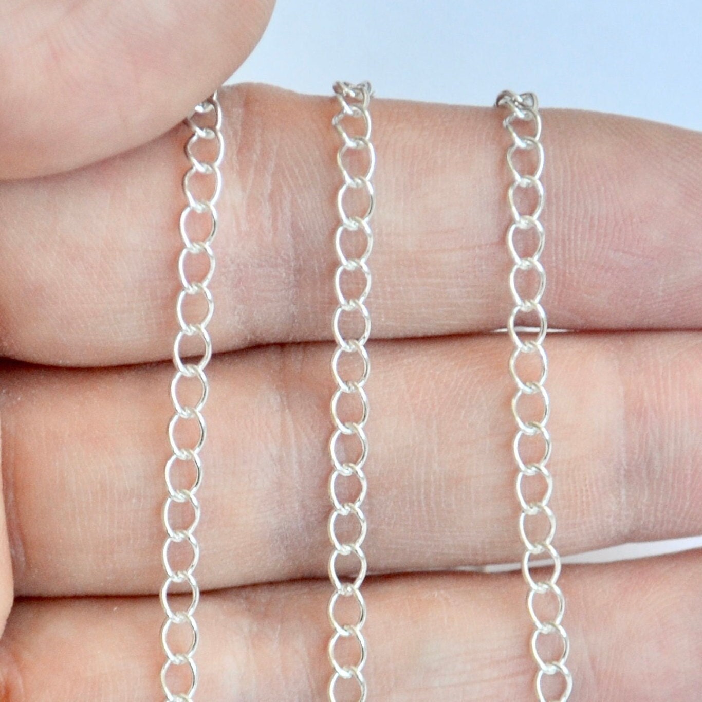 Silver extender chain held between fingers against a light background