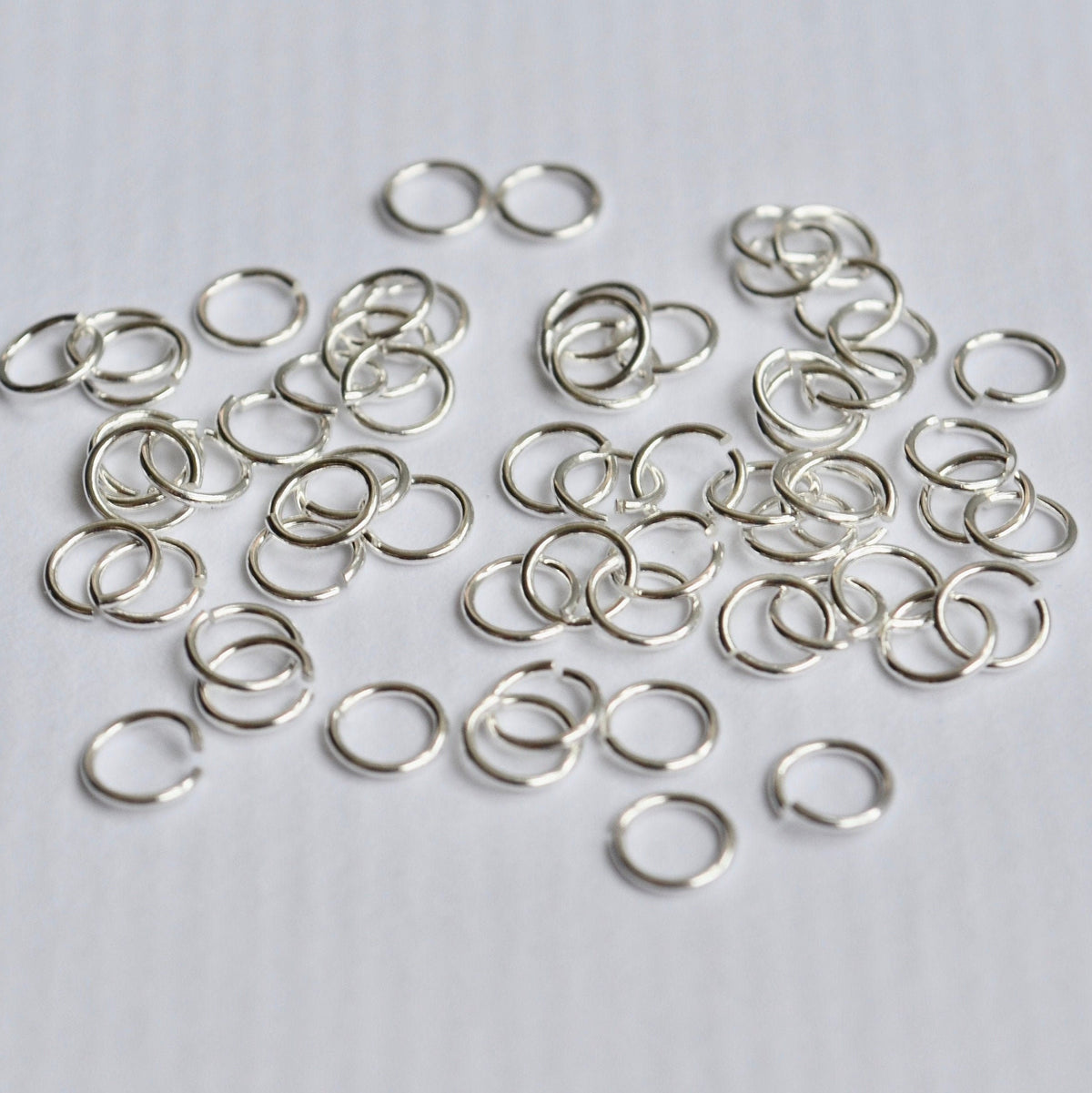 Small silver jump rings on a light gray background