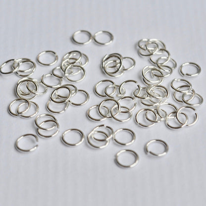 Small silver jump rings on a light gray background