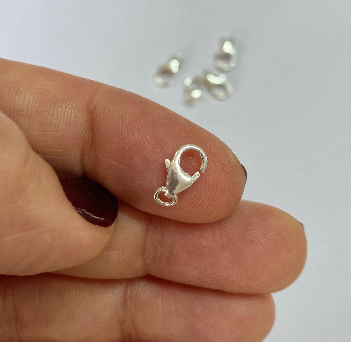 A silver lobster clasp with a small attached loop, held between a person's fingers against a plain light background.