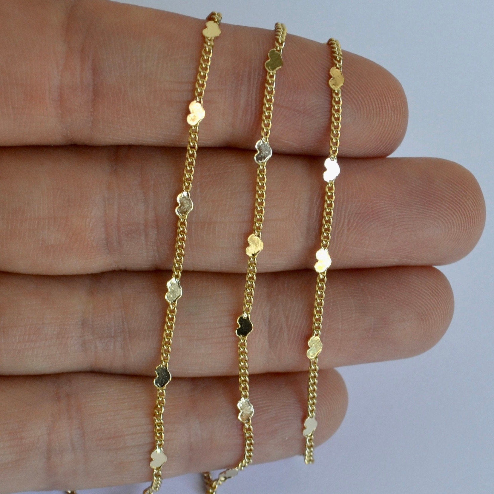 Three gold necklaces with dainty chain with tiny hearts on a hand against a white background