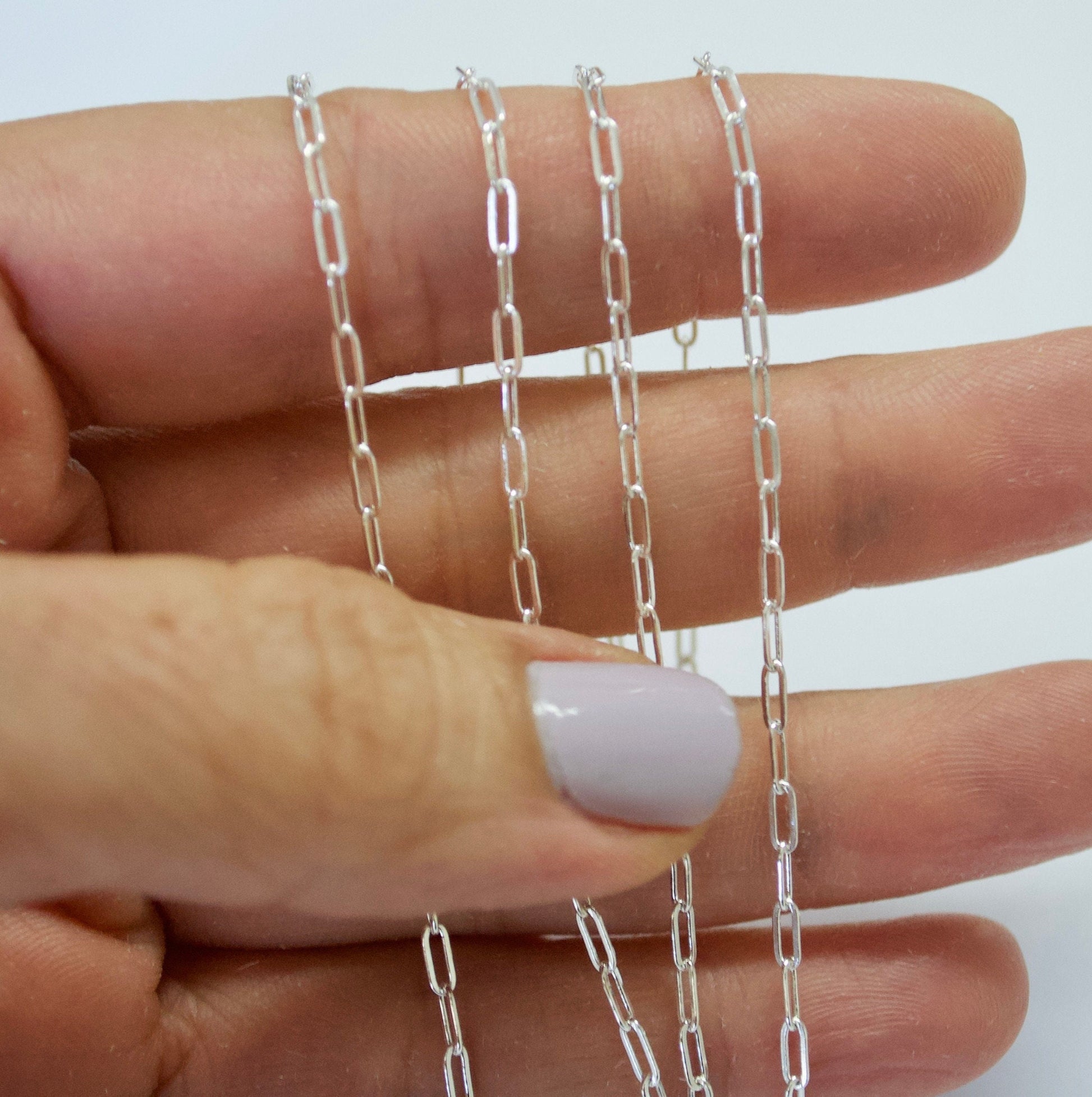Silver paper clip chain held between fingers against a white background